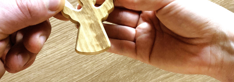 Zwei Hände von verschiedenen Personen, die gemeinsam einen Holzengel halten